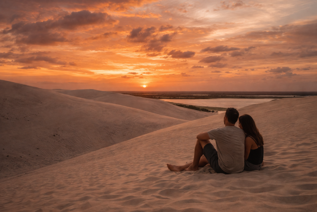 casal sentado nas dunas de jericoacoara assistindo ao pôr do sol romântico