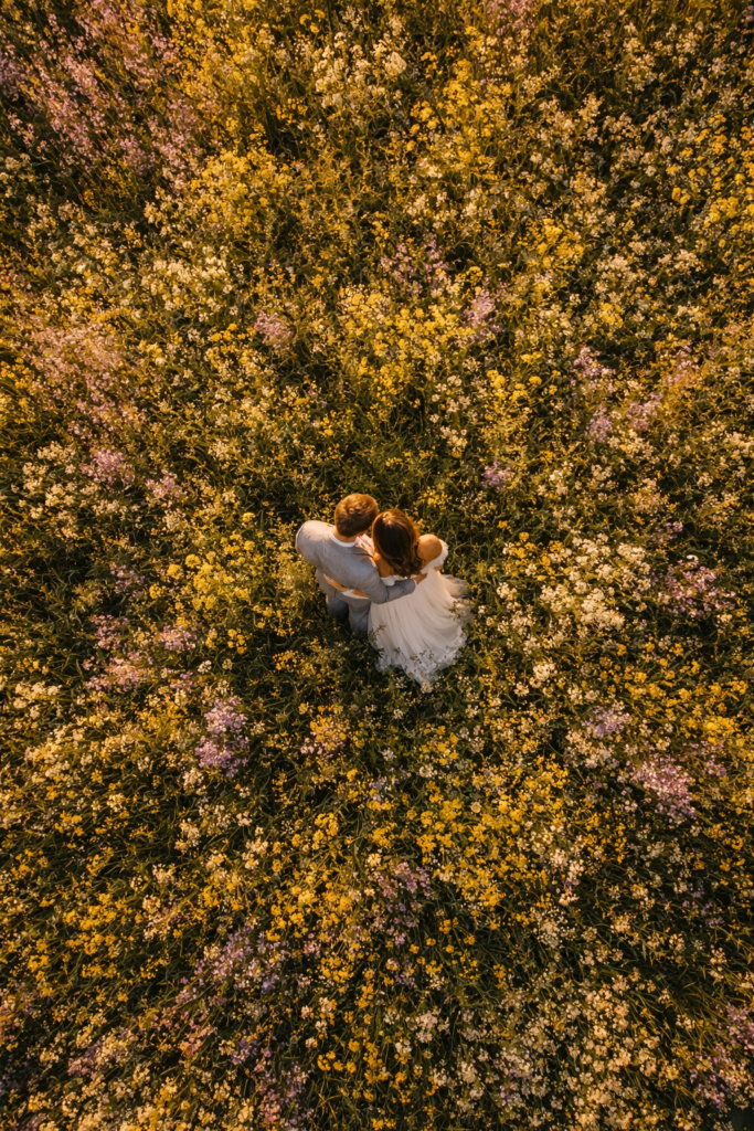 Casal de noivos visto de cima por drone em campo de flores silvestres ao entardecer
